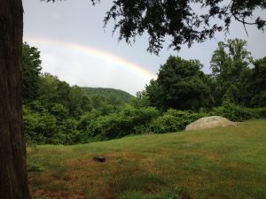 Grass with hill and rainbow behind on property.