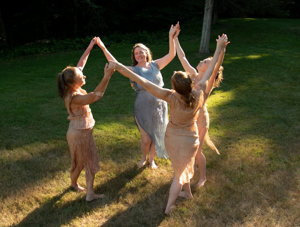 4 dancers holding hands aloft and looking joyful
